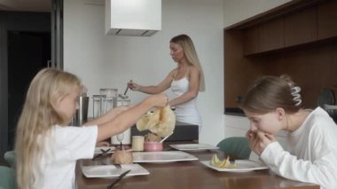 Bir anne, üç mutlu kızı birlikte yemek yerken, sevgi ile lezzetli krepler hazırlar ve servis eder. Çağdaş bir ev mutfağında sıcak aile anları ve kaynaşma.