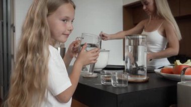 En küçük kızıyla ilgilenen kız kardeşleri için mutfakta su dolduruyor, ev işlerine yardım etmeyi öğreniyor. Annem gururla kahvenin tadını çıkartıyor. Kardeş sevgisinin ve aile bağının altını çiziyor..