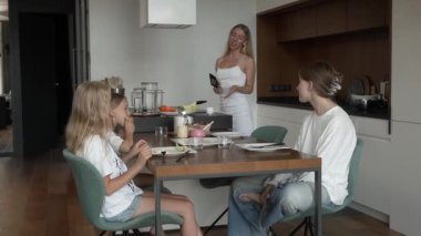 Bir anne yemek masasında krep yerken üç kızıyla sohbet eder. Modern mutfağındaki ev yapımı kahvaltı sırasında mutlu aile ilişkileri ve iletişim..
