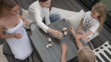 Teras masasında eşsiz tahta bloklarla oynayan bir anne ve üç kızın el manzarası. Takım çalışmalarını ve aile eğlencelerini gösteren bir kuleyi yeniden inşa ediyorlar..