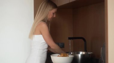 Modern bir mutfak lavabosunda duran bir kadın titizlikle taze mantar mantarlarını yıkıyor. Mantarları musluk suyunun altında duruluyor ve yemek için gurme malzemesi hazırlıyor..