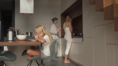 Küçük kız, ablası tabağını temizleyip kaldırırken masada mısır yiyor. Annem mutfakta taze bir salata hazırlıyor. Aile çalışmalarını ve günlük rutinlerini gösteriyor..