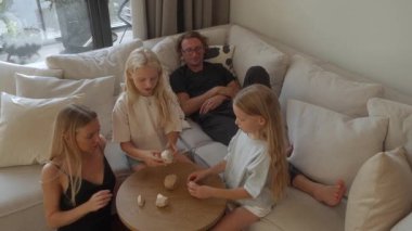 İki küçük kızı olan bir aile evde güzel vakit geçirir. Anne ve kızları sehpanın üzerindeki tahta blokları kullanarak dikkatlice bir kule inşa ederken, baba da kanepeden izliyor ve dinleniyor..