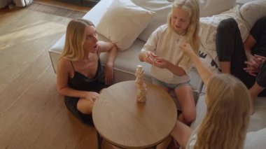 Bir aile (ebeveynler ve iki kızı) evde yaratıcı bir ahşap istifleme oyunu oynarken neşeli ve odaklanmış bir anı paylaşır. Dikkatlice bir kule inşa ederler, denge ve beceriyi test ederler, birlikte öğrenirler..