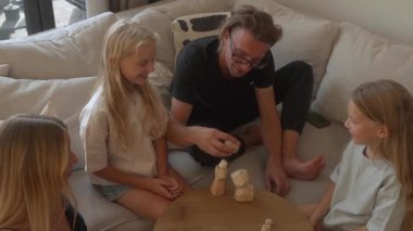 İki küçük kızı olan bir aile ahşap denge taşlarıyla oynar. Eğitici bir istifleme oyunu. Aileler ve çocuklar bir kule inşa eder, kahkahaları paylaşırlar ve evde vakit geçirmenin tadını çıkarırlar..