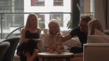 Babam sırayla uzun tahta bir kule inşa ediyor. Destekleyici eşi ve iki kızı, bu heyecan verici aile oyunu gecesinde onu dikkatle izliyor, gülümsüyor ve tezahürat yapıyor..