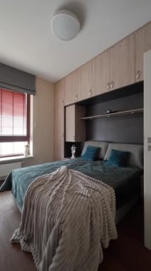 Geniş bir pencerenin yanındaki yatağı çerçeveleyen hafif ahşap kaplamalı modern yatak odası. Yumuşak tekstil, ahşap panjurlar, saksı bitkisi ve ahşap döşemeler bu organize, davetkar iç mekanı tamamlıyor..