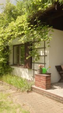 Güzel bir kır evi dış görünüşü ve güneşli bir bahçesi var. Beyaz duvarlar, tırmanan yeşil bitkiler, ahşap panjurlar, su dolu tuğla bir heykel ve dışarıda dinlenmek için bahçe mobilyaları.