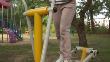 Açık hava eliptik üzerinde ilişki kurulabilir bir kadın, fitness hedeflerine odaklanmış, tüm vücudunu yukarı doğru bir kamera tepsisiyle yakalamış. Aktif ve sağlıklı kalmak için gösterdiği azim bu park çalışmasında açıkça görülüyor..