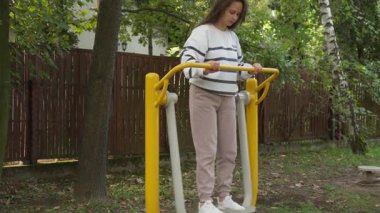 Spor kıyafetleri içinde aktif bir kadın halka açık bir parkta spor salonunda spor yapmak için hava yürüyüşü makinesi kullanıyor. Kardiyo çalışması yapıyor. Spor aletlerinin fiziksel aktivitelerinin keyfini çıkarıyor..