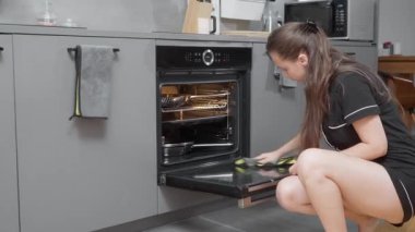 Pijamalı genç bir kadın entegre fırınının cam kapısını özenle bir bezle temizliyor. Ev işlerini yapıyor. Mutfak aletlerinin bakımlı ve hijyenik olmasını sağlıyor..