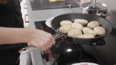 Kadın pirzola dağıtmak için çubuksuz bir tavayı sallıyor, sonra onu indüksiyon sobasının üzerine yerleştiriyor ve pişirmeye başlamak için kapakla kapatıyor. Bu yöntem köftelerin iyice pişmesine yardımcı olur..