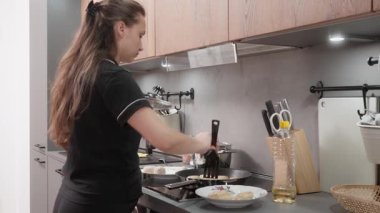 Kadın indüksiyon sobasında çubuksuz tavada kızaran pirzolaları dikkatlice kontrol ediyor. Seçilmiş olanları çevirmek için bir spatula kullanıyor. Ev aşçılığı süreci.