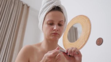 Kafası havluya sarılı bir kadın tırnak uçlarını kullanarak derinden tırnak bakımı yapar. Yatak odasındaki bu odaklanmış bakım ritüeli titizlikle el ve tırnaklarının bakımını sağlıyor..