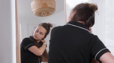 Pijamalı bir kadın uzun saçlarını aynanın önünde elektrikli saç stilisti kullanarak şekillendiriyor. Güne başlamadan önce saç stili yaratmaya odaklanmış..