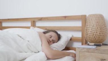 Yataktaki kadın, akıllı telefon alarmı ile uyandı. Uykulu bir şekilde cihaza uzanıyor, bildirimi kontrol ediyor, sonra da kestiriyor, güne başlamadan önce biraz daha uyumak istiyor..