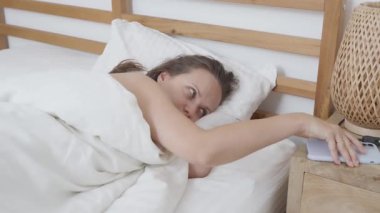 Yatakta genç bir kadın, akıllı telefon alarmıyla uyandı, cihaza uzandı, alarm verdi, sonra da uykulu gözlerini ovuşturup, rahat yatak odasında dinlenmeye çalıştı..