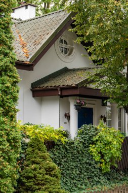 Büyüleyici geleneksel bir ev girişi sütunlu verandasının üzerinde kendine özgü yuvarlak bir tavan arası penceresi içerir. Yoğun sarmaşık ve yemyeşil gözlerden uzak, resim gibi bir görünüş yaratır..