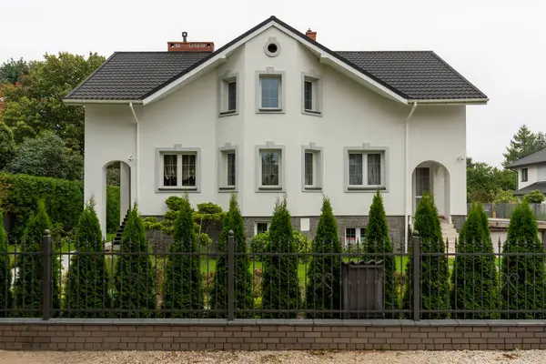 Metal çitlerin ve yeşil çitlerin arkasında bir banliyö evi, aile yaşamı için güvenli ve özel bir ortam sunuyor. Bu kurulum, ev sahipliği ve tenha bir yaşam tarzını ön plana çıkarıyor.