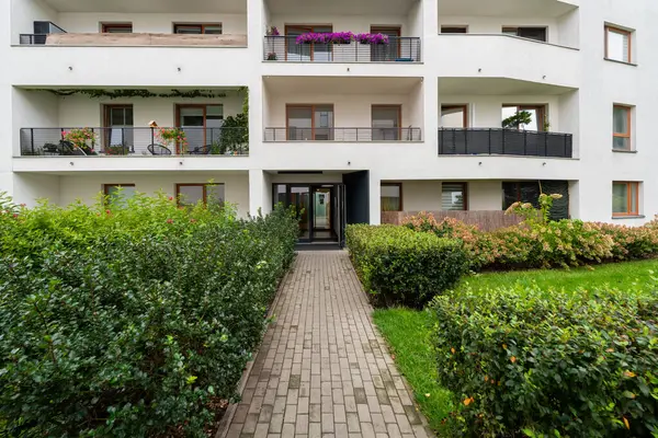 Çimlerin ve çayırların arasındaki patika modern apartman girişine çıkıyor. Bu peyzaj yaklaşımı çağdaş yerleşim birimlerine hoş geldin ve estetik erişim sunuyor..