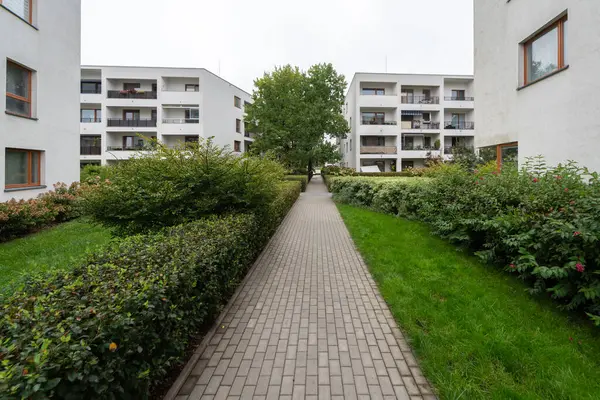 Çağdaş bir Avrupa yerleşim alanının peyzajlı avlusundan geçen bir patika. Çitlerle ve çimlerle çevrili olan bina binalarını birbirine bağlıyor ve toplumsal yeşil bir alan oluşturuyor..