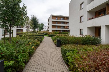 Peyzajlı yollar bu modern kompleks avludan geçiyor. Yoğun çalılar, süs otları ve apartman binaları arasında kaldırımlar oluşturan ağaçlar mevsimlik renkler sergiliyor..