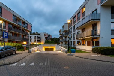 Modern bir konut kompleksinin yeraltı garaj girişi, alacakaranlıkta aydınlandı. Oturanlara elverişli, güvenli park yeri, bakımlı zemini olan konforlu bir daire sunuyor..