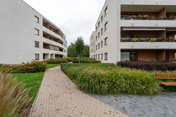 Modern bir konut kompleksinin peyzajlı avlusunda kıvrımlı kaldırım yolu. Çimenlerle, süslü otlarla, çalılarla çevrili bina sakinleri için sakin bir ortam sunuyor..