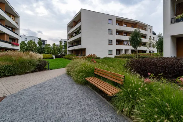 Modern konut kompleksi avlusu detaylı peyzaj mimarisini gözler önüne seriyor. Dokulu asfalt döşeme, süs otları, çiçek açan çalılar ve banklar sakinler için davet edici eğlence alanları oluşturur..