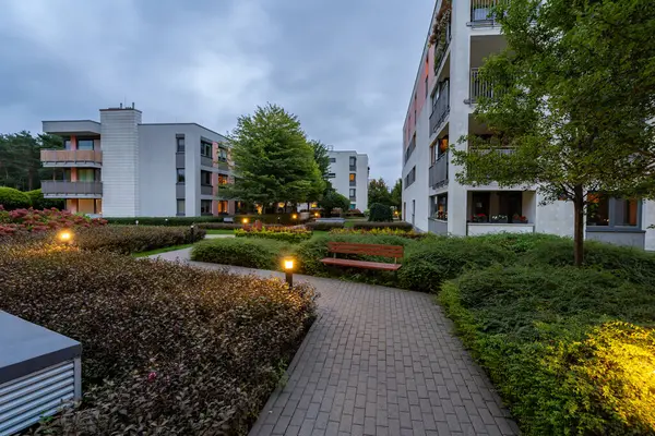 Modern bir yerleşim yerinin bahçesinde sakin bir akşam ortamı. Aydınlatılmış yollar ve aydınlatma huzur ortamını güçlendirir, karanlık çöktükten sonra açık havada karşılama alanı yaratır..