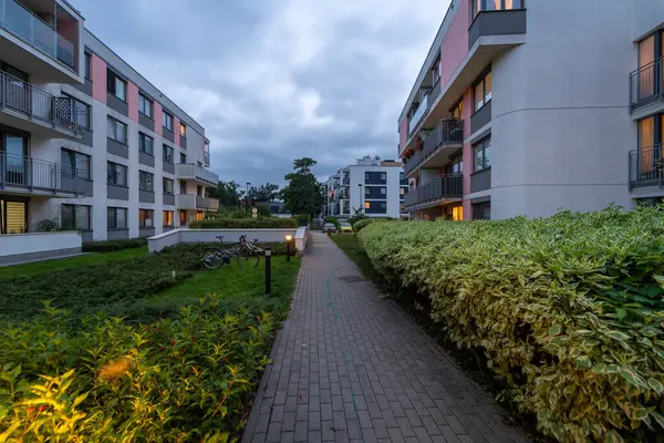 Peyzajlı zemini ve aydınlık yolları olan modern bir konut kompleksi. Apartman binaları görünür, yeşil bitkilerin arasında ortak alana park edilmiş bir bisiklet var..