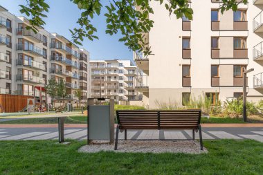 Güzel bir yaz gününde konutlarda iyi donanımlı ortak alanlar. Park bankı ve çöp tenekesi çocukların oyun parkının yanında rahat bir yürüyüş için konfordur..