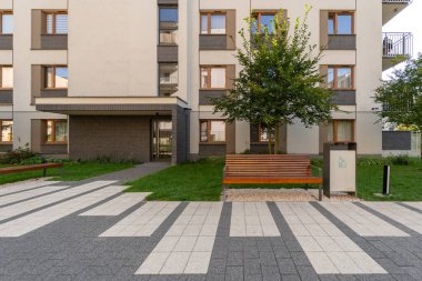 Dekoratif ve desenli kaldırımlı modern bir konut kompleksinde kamusal alan. Ahşap banklar binanın yanındaki manzaralı avluda yaşayanlara oturma olanağı sağlıyor..