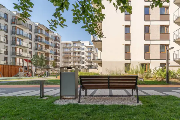 Güzel bir yaz gününde konutlarda iyi donanımlı ortak alanlar. Park bankı ve çöp tenekesi çocukların oyun parkının yanında rahat bir yürüyüş için konfordur..