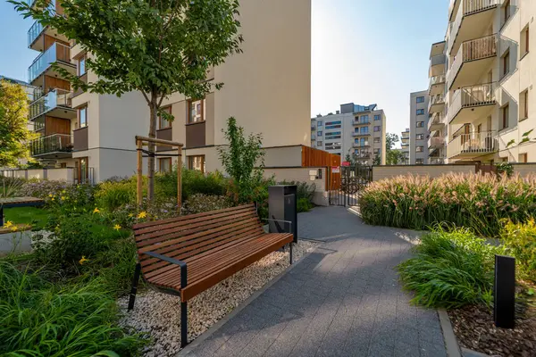 Modern bir konut kompleksinin içinde halka açık bir park. Bir ahşap bank ve bir çöp tenekesi peyzaj yeşil bitkiler arasında yer alır, süs otları ve çiçekler de dahil.