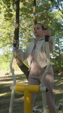 Odaklanmış bir kadın eliptik bir makine üzerinde çalışıyor, azim ve dayanıklılık gösteriyor. Halk parkındaki kardiyo eğitimi motivasyon ve irade konsepti..