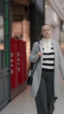 Zarif bir kadın alışveriş merkezinden geçiyor, vitrinlere bakıyor. Vitrinlere bakıyor, vitrinlere bakıyor ve alışveriş merkezinin atmosferinin tadını çıkarıyor..