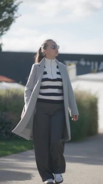 Şık paltolu ve güneş gözlüklü kendine güvenen bir kadın şehir caddesinde yürüyor. Bu modern şehir modası, sokak tarzı ve başarılı, bağımsız bir yaşam tarzı..