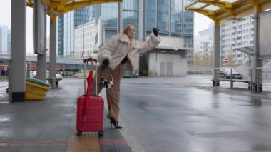 Kırmızı bavullu sabırsız bir kadın ıslak bir caddede taksi çağırmaya çalışıyor. Bir nakliye merkezinde bekliyor. Seyahat planındaki gecikme onu hayal kırıklığına uğratmış..