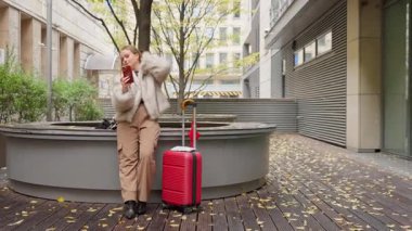 Bagajlı bir bayan gezgin, görüntüsünü kontrol etmek için telefonunun kamerasını ayna olarak kullanır. Seyahat haberlerini paylaşmak için video araması yapmadan önce kendini hazırlıyor..