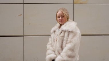 Lüks kürklü güzel bir manken bir moda fotoshoot için poz veriyor. Modern, minimalist bir duvara karşı yürür ve döner. Şık bir şehir tarzı video yaratır..