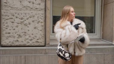 Şık, sahte kürklü genç sarışın kadın bir şehir caddesinde duruyor, yolunu bulmak için bir kağıt haritaya danışıyor. Odaklanmış görünüyor, bir turistin şehir ortamını keşfetme deneyimini somutlaştırıyor.