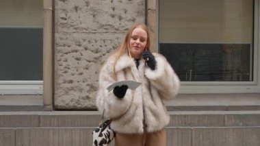 Sahte kürklü sarışın bir kadın, elinde kağıt bir harita tutarken bir şehir caddesinde cep telefonuyla konuşuyor. Aktif olarak iletişim kuruyor, yönleri tartışıyor ya da seyahat deneyimini paylaşıyor..