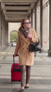 Bagajlı bir bayan turist, kolonları olan güzel bir atari salonunda yürüyor. Klasik bir Avrupa şehrini keşfeden şık bir gezgin, yolculuğunda tarihi mimarinin yanından geçiyor..