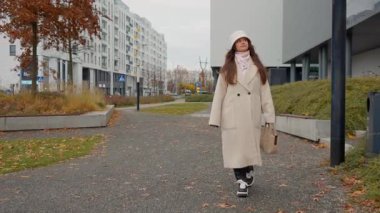 Sonbaharda yeni bir yerleşim bölgesinin yeşil alanlarında gezinen genç bir kadın. Şehir sakini modern bir Avrupa şehrinde apartmanının yakınında yürüyüş yapıyor..