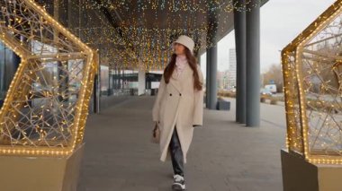 Genç bir kadın, kış tatili için dekore edilmiş bir şehirde neşeli bir atmosferin tadını çıkarıyor. Güzel Noel ışıklarının ve dekorasyonların yanından geçerken sezonun sihrini hissediyorum..