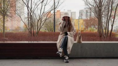 Şehir parkındaki bankta oturan ve cep telefonuyla konuşan genç bir kadın. Sonbahar boyunca dışarıda dinlenirken, cep telefonuyla hoş bir sohbete girişir..