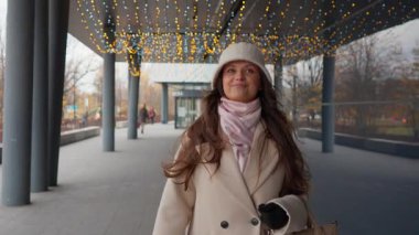 Neşeli bir kadın, bayram ışıklarıyla süslenmiş bir alışveriş merkezinde yürüyor. Mutlu müşteri gülümsüyor, Noel indirimi sezonunun sihirli ve ruhuyla dolu..