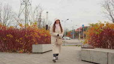 Şapkalı ve paltolu güzel bir kadın halka açık bir parkta kaldırımda yürüyor. Çağdaş bir kentsel ortamda serin bir sonbahar gününde keyifli bir gezinti yapan bir insan..