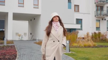 Genç bir asistan, elleri ceplerinde özel bir apartman dairesi avlusunda yürüyor. Sakin bir sonbahar gününde modern kapılı topluluğunun rahatlığı ve güvenliğinin tadını çıkarıyor..